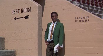 Movie still from “Hickey & Boggs” (1972), directed by Robert Culp – A man in a green jacket and a brown tie standing in front of a wall; Medium shot, Low angle