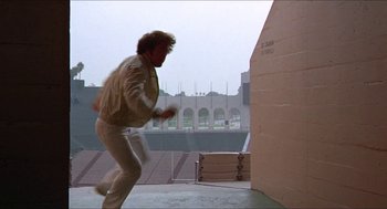 Movie still from “Hickey & Boggs” (1972), directed by Robert Culp – A man running on the ground in front of an arena; Wide shot, Low angle