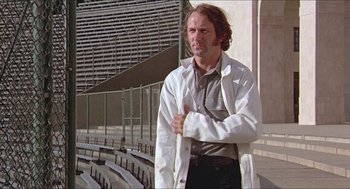 Movie still from “Hickey & Boggs” (1972), directed by Robert Culp – A man standing in front of a bleachers wearing a lab coat; Medium shot, Low angle