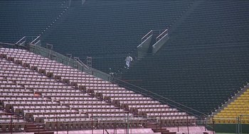Movie still from “Hickey & Boggs” (1972), directed by Robert Culp – A man riding a skateboard down the side of an empty stadium; Extreme Wide shot, High angle