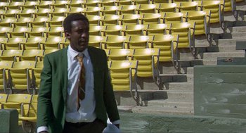 Movie still from “Hickey & Boggs” (1972), directed by Robert Culp – A man in a green suit and tie standing in front of yellow seats; Medium shot, Low angle