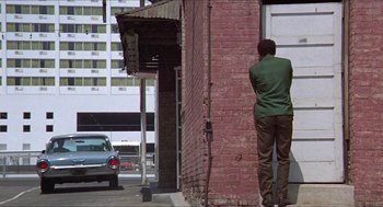 Movie still from “Hickey & Boggs” (1972), directed by Robert Culp – A man standing on the side of a brick building; Wide shot, Low angle