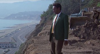 Movie still from “Hickey & Boggs” (1972), directed by Robert Culp – A man in a green jacket and brown pants standing on a hill; Wide shot, Low angle