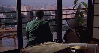 Movie still from “Hickey & Boggs” (1972), directed by Robert Culp – A man sitting in front of a window looking out at a city skyline; Wide shot, High angle