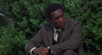 Movie still from “Hickey & Boggs” (1972), directed by Robert Culp – A man in a suit and tie sitting next to a bush; Close Up shot, Low angle