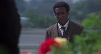 Movie still from “Hickey & Boggs” (1972), directed by Robert Culp – A man in a suit and tie standing in front of flowers; Close Up shot, Low angle