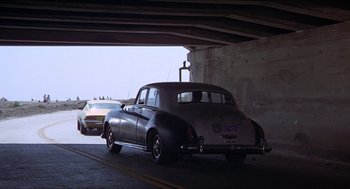 Movie still from “Hickey & Boggs” (1972), directed by Robert Culp – An old car is parked under a bridge; Wide shot, Low angle
