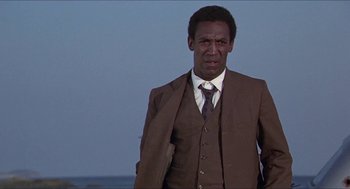 Movie still from “Hickey & Boggs” (1972), directed by Robert Culp – A man in a suit and tie standing in front of a body of water; Medium shot, Low angle