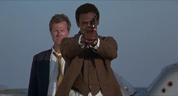 Movie still from “Hickey & Boggs” (1972), directed by Robert Culp – A man holding a gun while standing next to another man; Medium shot, Low angle