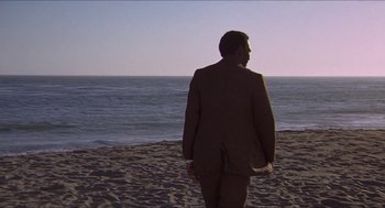 Movie still from “Hickey & Boggs” (1972), directed by Robert Culp – A man in a suit standing on the beach looking out at the ocean; Extreme Wide shot, Over the shoulder angle