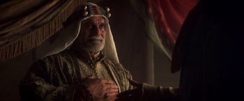 Movie still from “Hidalgo” (2004), directed by Joe Johnston – An old man wearing a headdress and holding his hands over his chest; Close Up shot, Over the shoulder angle
