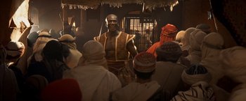 Movie still from “Hidalgo” (2004), directed by Joe Johnston – A man is standing in front of a group of people; Medium shot, Over the shoulder angle