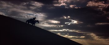 Movie still from “Hidalgo” (2004), directed by Joe Johnston – A person riding a horse on top of a hill under a cloudy sky; Extreme Wide shot, Low angle