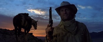 Movie still from “Hidalgo” (2004), directed by Joe Johnston – A man holding a gun while standing next to a horse; Medium shot, Low angle