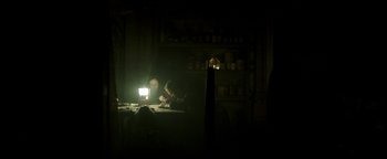 Movie still from “Hidden” (2015), directed by Ross Duffer – A man sitting at a table in a dark room; Wide shot, High angle