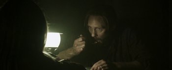 Movie still from “Hidden” (2015), directed by Ross Duffer – A man with a beard is sitting in a dark room; Close Up shot, Over the shoulder angle