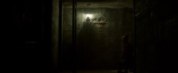 Movie still from “Hidden” (2015), directed by Ross Duffer – A person sitting in a dark room with a light shining on the wall; Extreme Wide shot, High angle