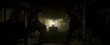 Movie still from “Hidden” (2015), directed by Ross Duffer – Two men sitting in a dimly - lit room next to a lamp; Wide shot, High angle