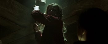 Movie still from “Hidden” (2015), directed by Ross Duffer – A young girl is holding a wooden stick in a dark room; Medium shot, Low angle