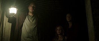 Movie still from “Hidden” (2015), directed by Ross Duffer – A man and a woman and a little girl standing in a dark room; Medium shot, Low angle