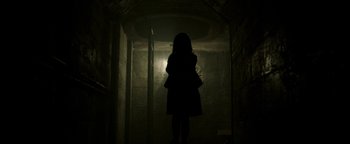 Movie still from “Hidden” (2015), directed by Ross Duffer – A woman standing in a dark room with her head turned to the side; Wide shot, Low angle