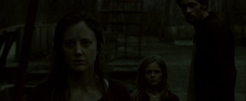 Movie still from “Hidden” (2015), directed by Ross Duffer – A woman standing next to a child in a dark room; Medium shot, Low angle