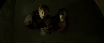 Movie still from “Hidden” (2015), directed by Ross Duffer – A man and a woman and a child in a dark room; Medium shot, Overhead angle