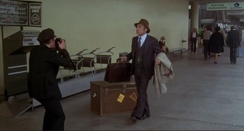 Movie still from “High Anxiety” (1977), directed by Mel Brooks – A man in a suit and hat walking through an airport; Wide shot, Over the shoulder angle