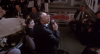 Movie still from “High Anxiety” (1977), directed by Mel Brooks – A man in a black suit is holding a microphone; Medium shot, High angle