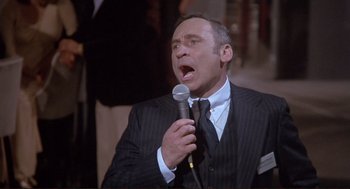 Movie still from “High Anxiety” (1977), directed by Mel Brooks – A man wearing a suit and tie holding a microphone; Medium shot, High angle