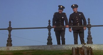 Movie still from “High Anxiety” (1977), directed by Mel Brooks – Two men in police uniforms standing next to each other; Wide shot, Low angle