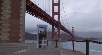 Movie still from “High Anxiety” (1977), directed by Mel Brooks – A man standing in front of a phone booth under the golden gate bridge in san francisco; Extreme Wide shot, Low angle