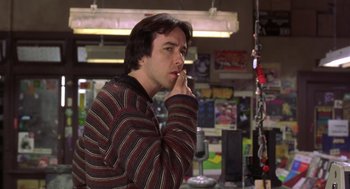 Movie still from “High Fidelity” (2000), directed by Stephen Frears – A man smoking a cigarette while wearing a striped sweater; Medium shot, Low angle