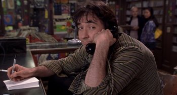 Movie still from “High Fidelity” (2000), directed by Stephen Frears – A man talking on a phone while sitting in a chair; Close Up shot, Low angle