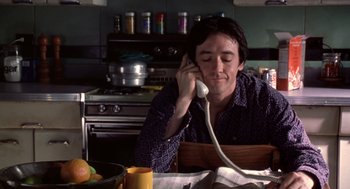 Movie still from “High Fidelity” (2000), directed by Stephen Frears – A man sitting at a table talking on a phone; Medium shot, Low angle