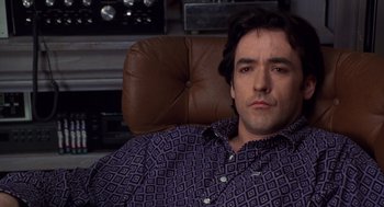 Movie still from “High Fidelity” (2000), directed by Stephen Frears – A person sitting in a chair wearing a shirt; Close Up shot, High angle