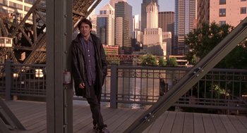 Movie still from “High Fidelity” (2000), directed by Stephen Frears – A man standing on a bridge in front of a city skyline; Wide shot, Over the shoulder angle