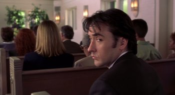 Movie still from “High Fidelity” (2000), directed by Stephen Frears – A man sitting in a pew in front of other people; Close Up shot, Low angle