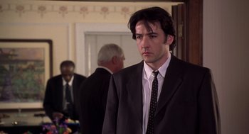 Movie still from “High Fidelity” (2000), directed by Stephen Frears – A man wearing a suit and tie standing in a room; Medium shot, Low angle