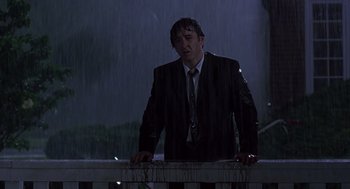 Movie still from “High Fidelity” (2000), directed by Stephen Frears – A man wearing a suit and tie standing in the rain next to a railing; Medium shot, Low angle