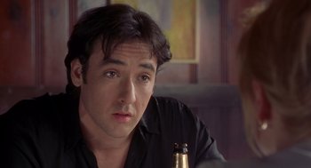 Movie still from “High Fidelity” (2000), directed by Stephen Frears – A person sitting at a table holding a beer; Close Up shot, Over the shoulder angle