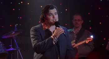Movie still from “High Fidelity” (2000), directed by Stephen Frears – A man in a suit is singing into a microphone; Medium shot, Over the shoulder angle