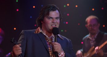 Movie still from “High Fidelity” (2000), directed by Stephen Frears – A man in a suit holding a microphone and making an angry face; Close Up shot, Over the shoulder angle