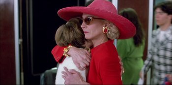Movie still from “High Heels” (1991), directed by Pedro Almodóvar – An older woman in a red hat hugging a younger woman; Close Up shot, Low angle