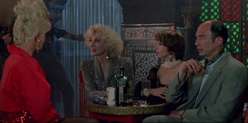 Movie still from “High Heels” (1991), directed by Pedro Almodóvar – Two women sitting at a table in front of a bottle; Medium shot, Over the shoulder angle