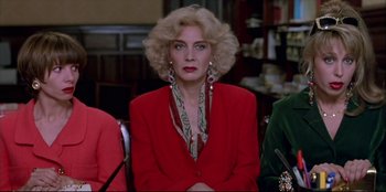 Movie still from “High Heels” (1991), directed by Pedro Almodóvar – A woman in a red jacket sitting in front of other people; Close Up shot, Low angle