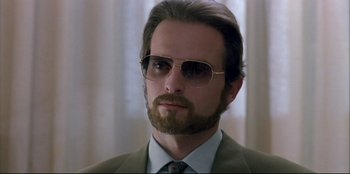 Movie still from “High Heels” (1991), directed by Pedro Almodóvar – A person wearing a suit and sunglasses; Close Up shot, Low angle