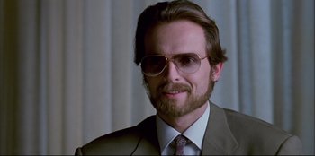 Movie still from “High Heels” (1991), directed by Pedro Almodóvar – A person wearing a suit and glasses; Close Up shot, Low angle