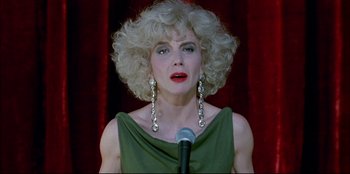 Movie still from “High Heels” (1991), directed by Pedro Almodóvar – A woman in a green dress is holding a microphone; Close Up shot, Low angle