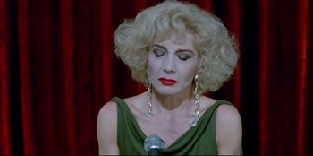Movie still from “High Heels” (1991), directed by Pedro Almodóvar – A woman in a green dress is singing into a microphone; Close Up shot, High angle